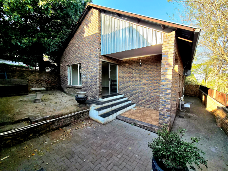 Rear view of a face brick house featuring a paved courtyard, sliding door access, and a covered patio area with tiled steps.