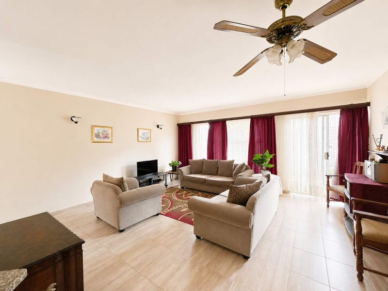 Spacious living room featuring neutral tiled flooring, a ceiling fan, and large sliding glass doors providing access to the outdoor area.