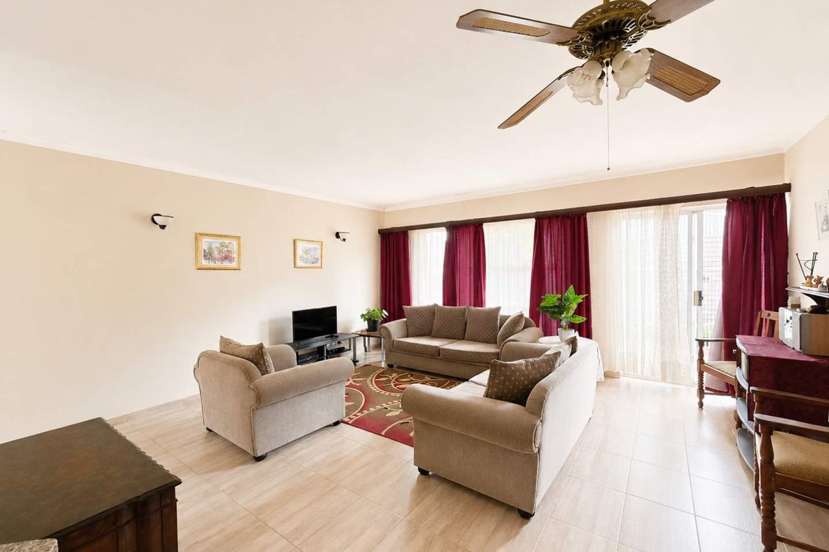 Spacious living room featuring neutral tiled flooring, a ceiling fan, and large sliding glass doors providing access to the outdoor area.