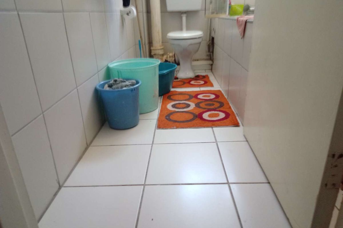 A functional bathroom featuring white ceramic wall and floor tiles, a standard toilet, and a bathtub with exposed plumbing.