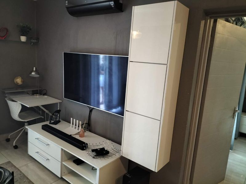 A living room area featuring a wall-mounted air conditioning unit, tiled flooring, and a tall built-in storage cabinet.