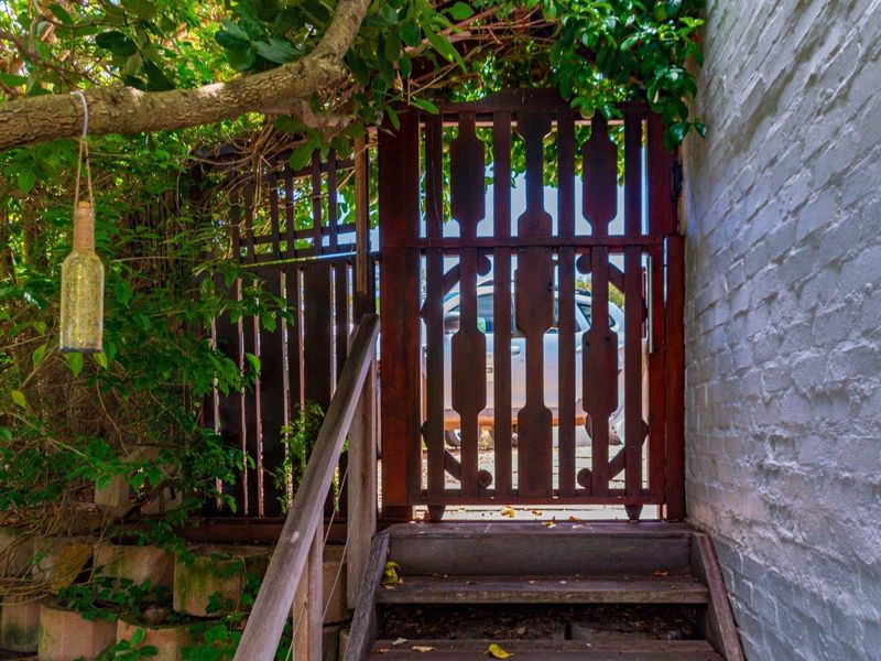 A weathered timber gate and staircase providing access to the property, framed by a painted brick wall and mature garden foliage.