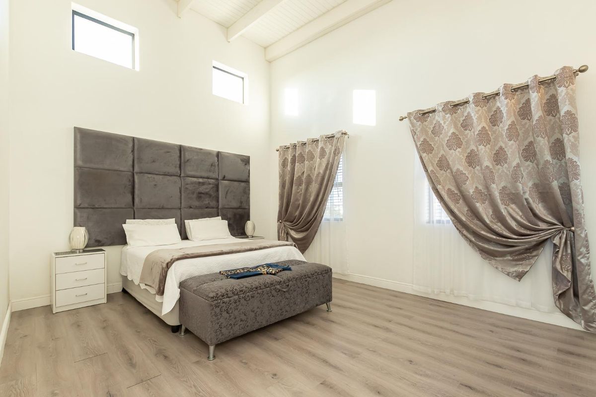 Spacious bedroom featuring high vaulted ceilings, light-toned laminate flooring, and a large upholstered feature headboard with clerestory windows for natural light.