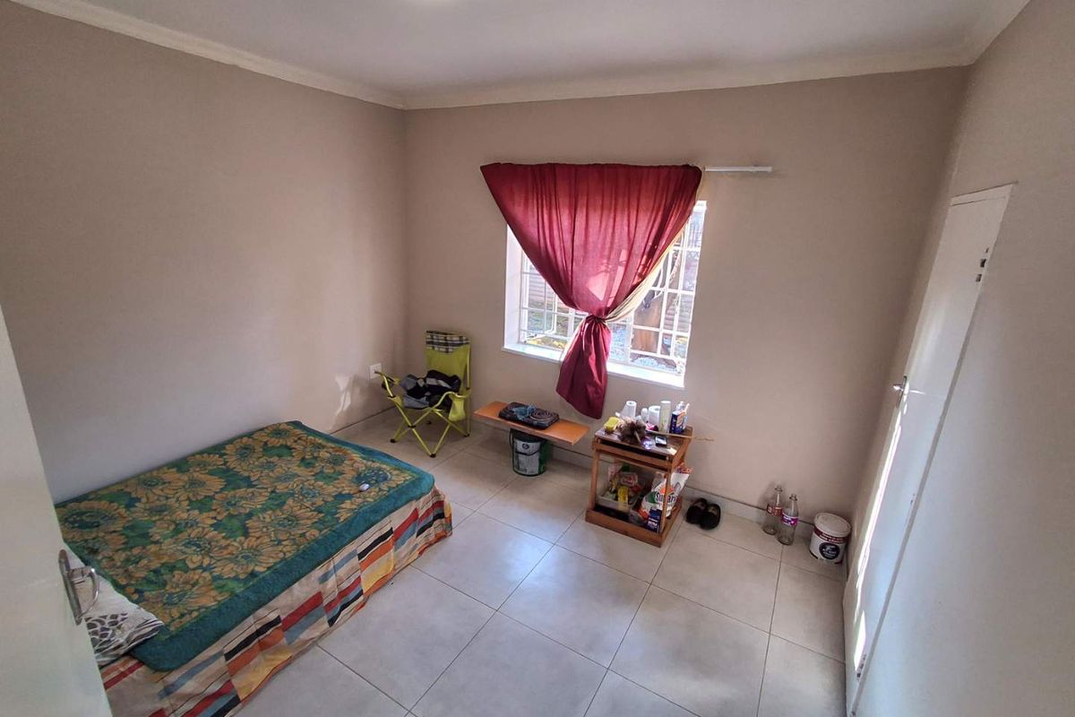 A simple bedroom featuring tiled flooring, neutral wall paint, and a window fitted with security bars.