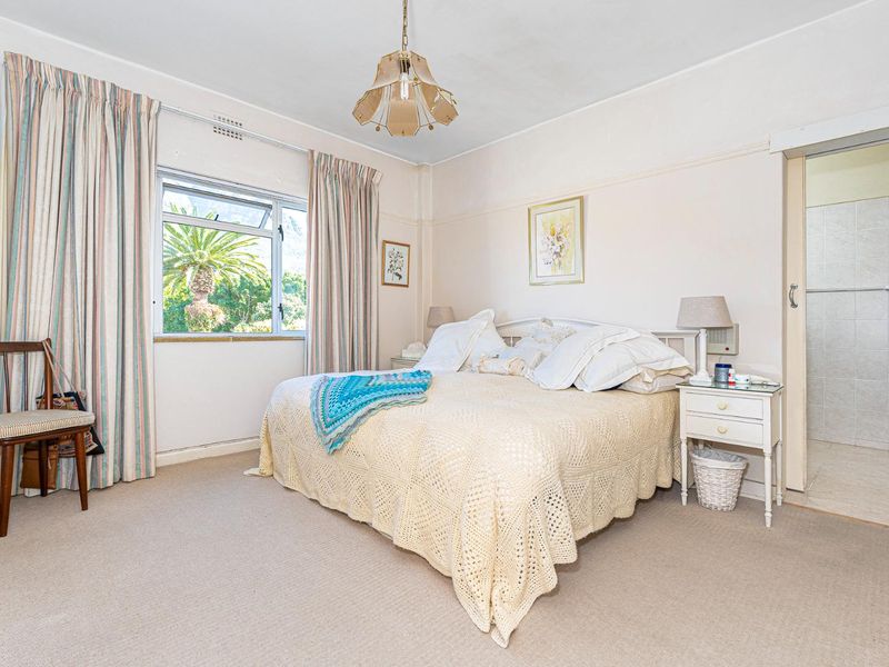 A well-proportioned bedroom featuring a picture rail, casement window, and an adjoining en-suite bathroom.