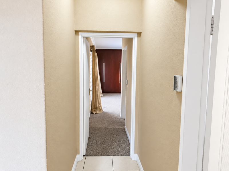 A clean, neutral-toned hallway leading into a bedroom area featuring built-in wooden cupboards and carpeted flooring.