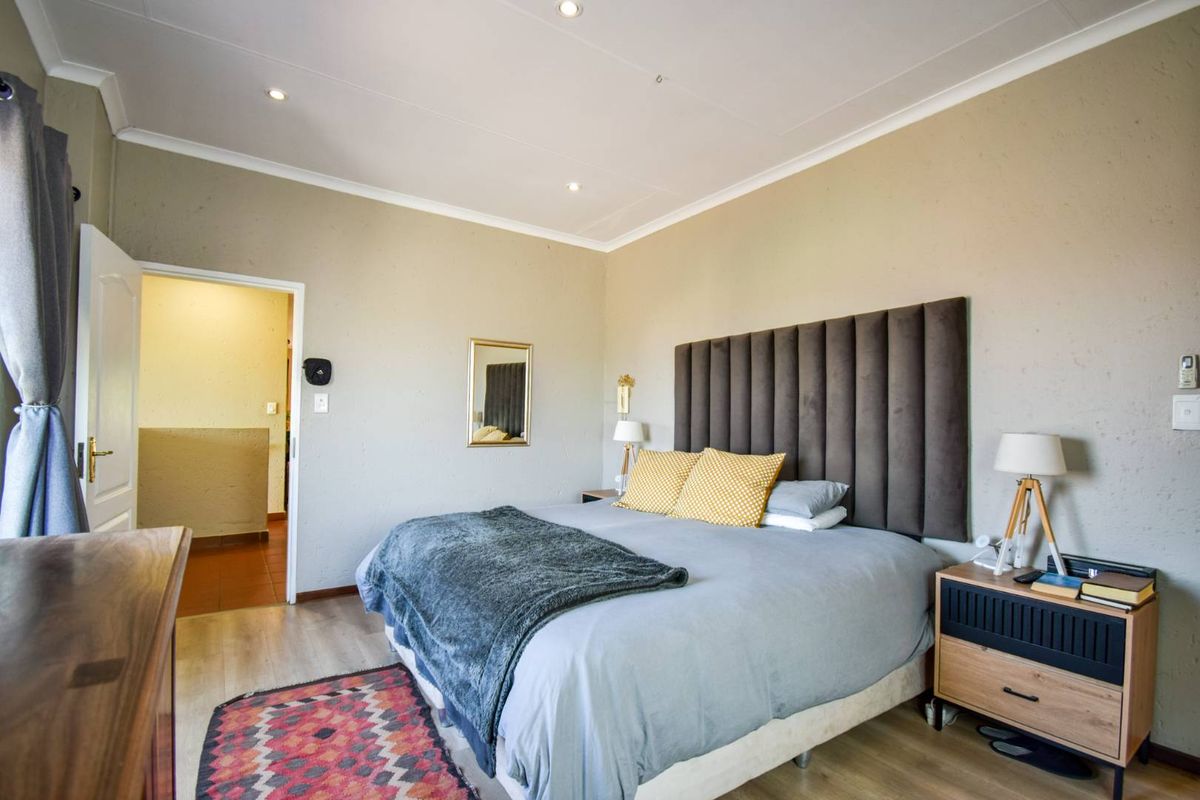 A well-maintained bedroom featuring neutral wall finishes, recessed ceiling lighting, and laminate flooring, with an adjoining doorway leading to an adjacent space.