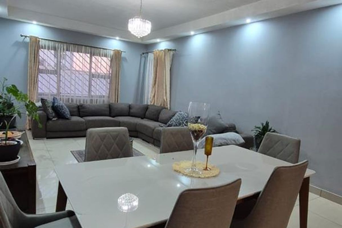 An open-plan living and dining area featuring tiled flooring, recessed downlighting, and a central crystal chandelier, creating a bright and functional living space.