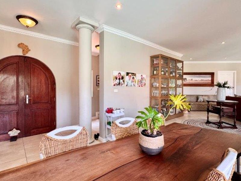 Spacious open-plan living area featuring tiled flooring, decorative ceiling cornices, recessed lighting, and a distinctive arched wooden double door entrance.