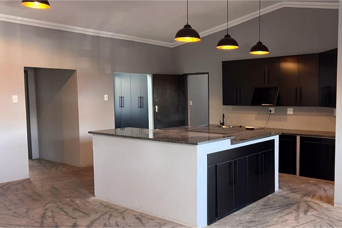 Modern kitchen featuring a central island with granite countertops, dark cabinetry, and pendant lighting, currently awaiting final flooring installation.