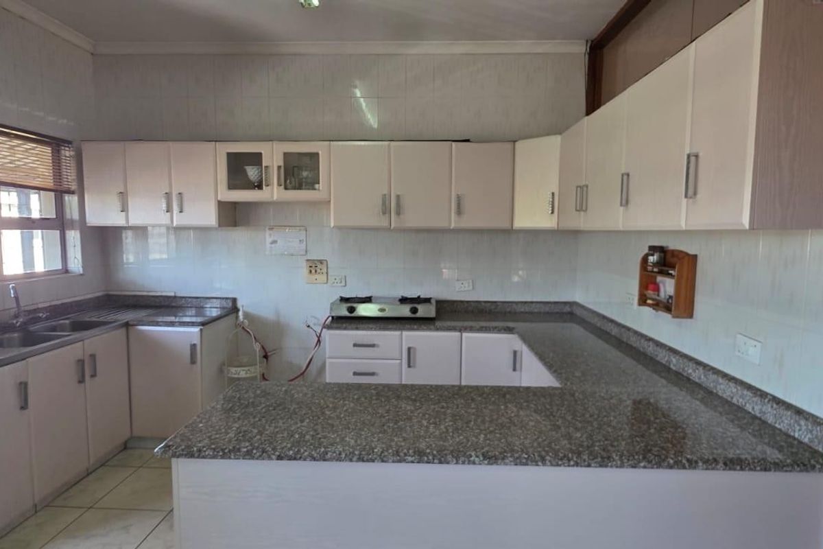 A functional kitchen featuring granite countertops, ample built-in cabinetry, a stainless steel sink, and a gas hob with tiled backsplash.