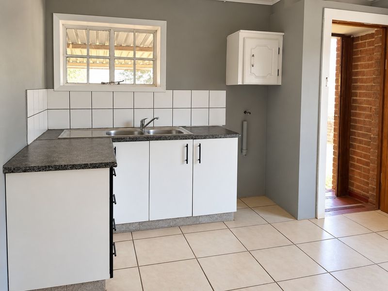 A clean, functional kitchen area featuring white cabinetry, a stainless steel double sink, tiled splashback, and neutral ceramic floor tiles.