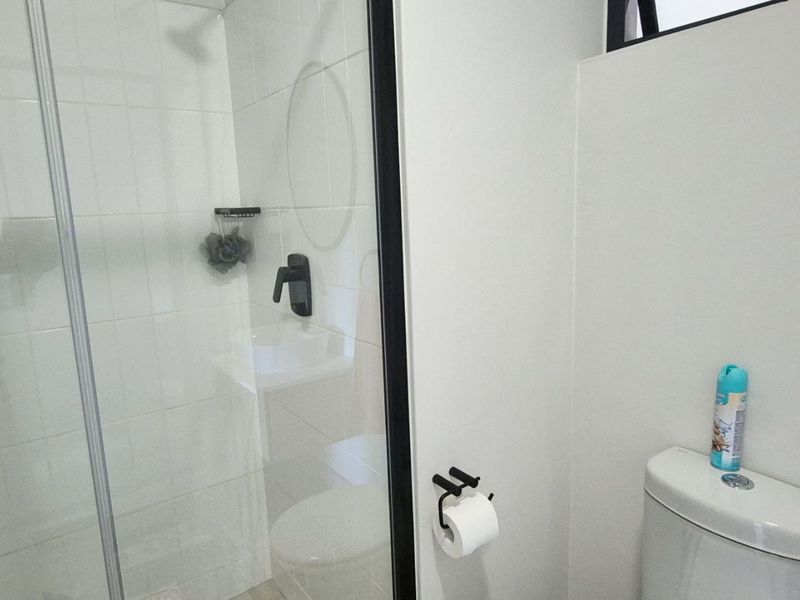 A clean, modern bathroom featuring a glass-enclosed shower, white wall tiles, and contemporary black fixtures.