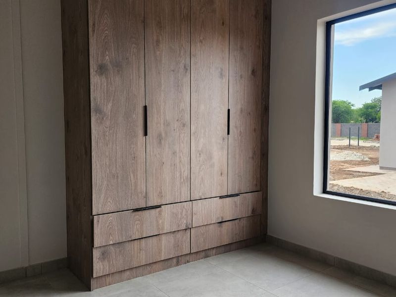 A bright, modern bedroom featuring high-quality wood-finish built-in cupboards and neutral floor tiles, offering a clean and contemporary living space.