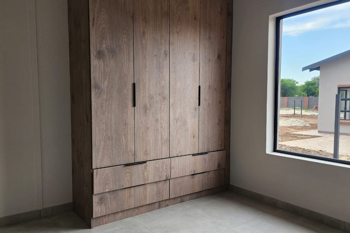 A bright, modern bedroom featuring high-quality wood-finish built-in cupboards and neutral floor tiles, offering a clean and contemporary living space.
