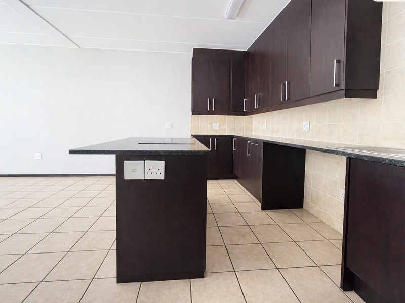 A clean, empty kitchen featuring dark wood cabinetry, granite countertops, a central island, and neutral tiled flooring.