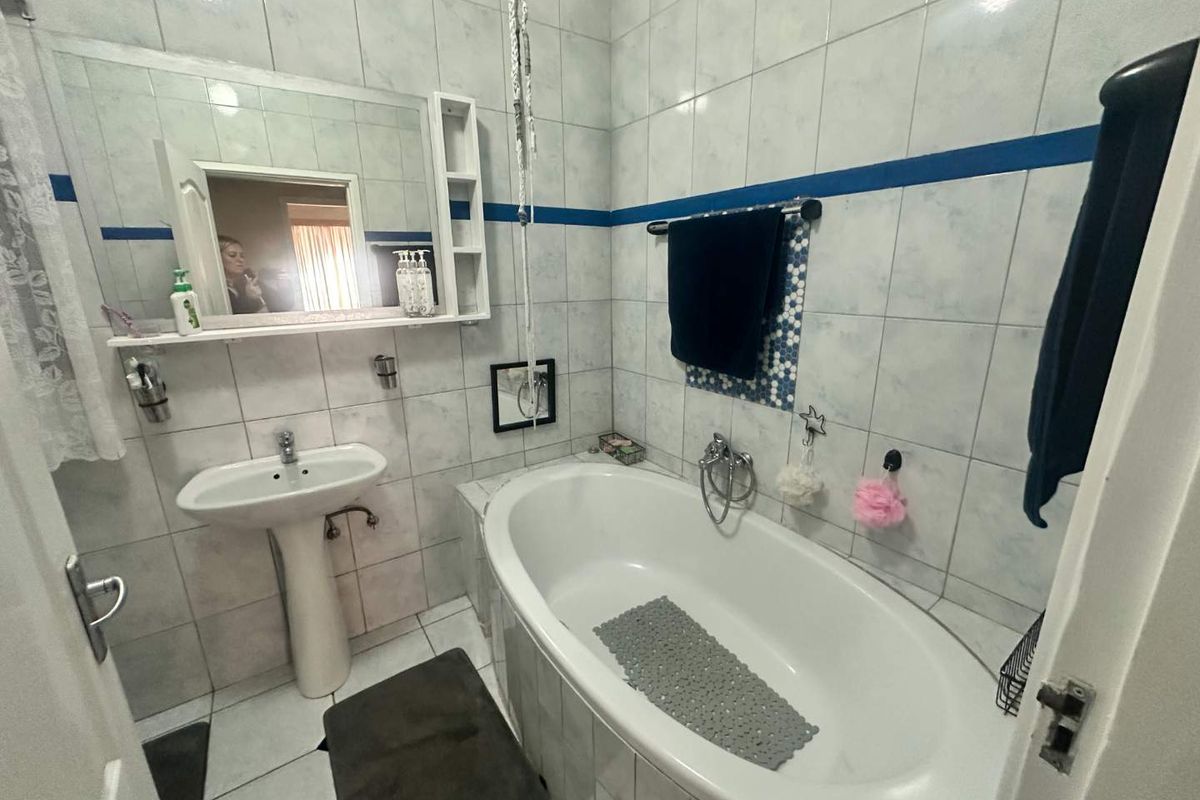 A functional bathroom featuring a pedestal sink, a built-in bathtub with shower mixer, and full-height wall tiling with a decorative blue accent border.