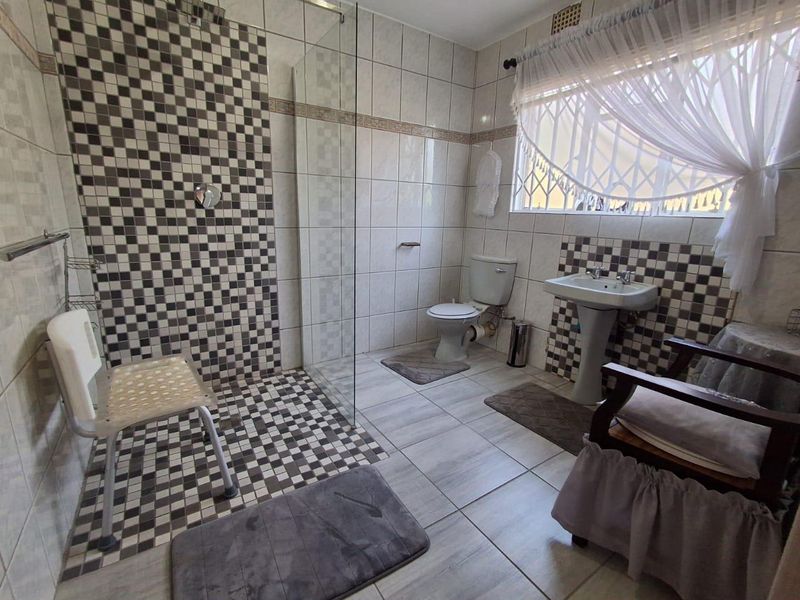 A functional bathroom featuring a walk-in shower with a glass screen, pedestal basin, toilet, and contrasting checkered wall tiling.