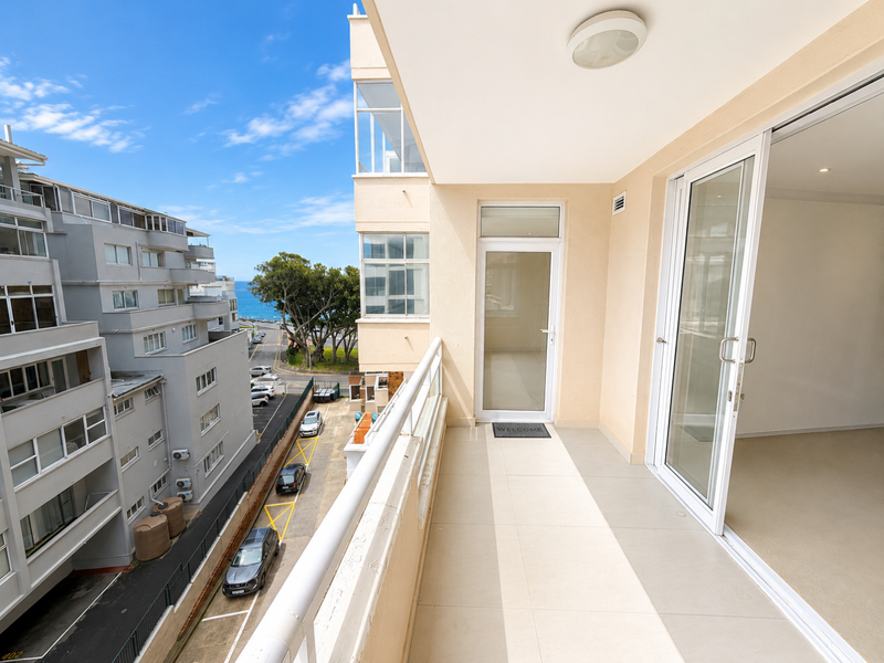 A clean, well-maintained balcony featuring tiled flooring, a safety railing, and glass sliding door access to the interior living space.