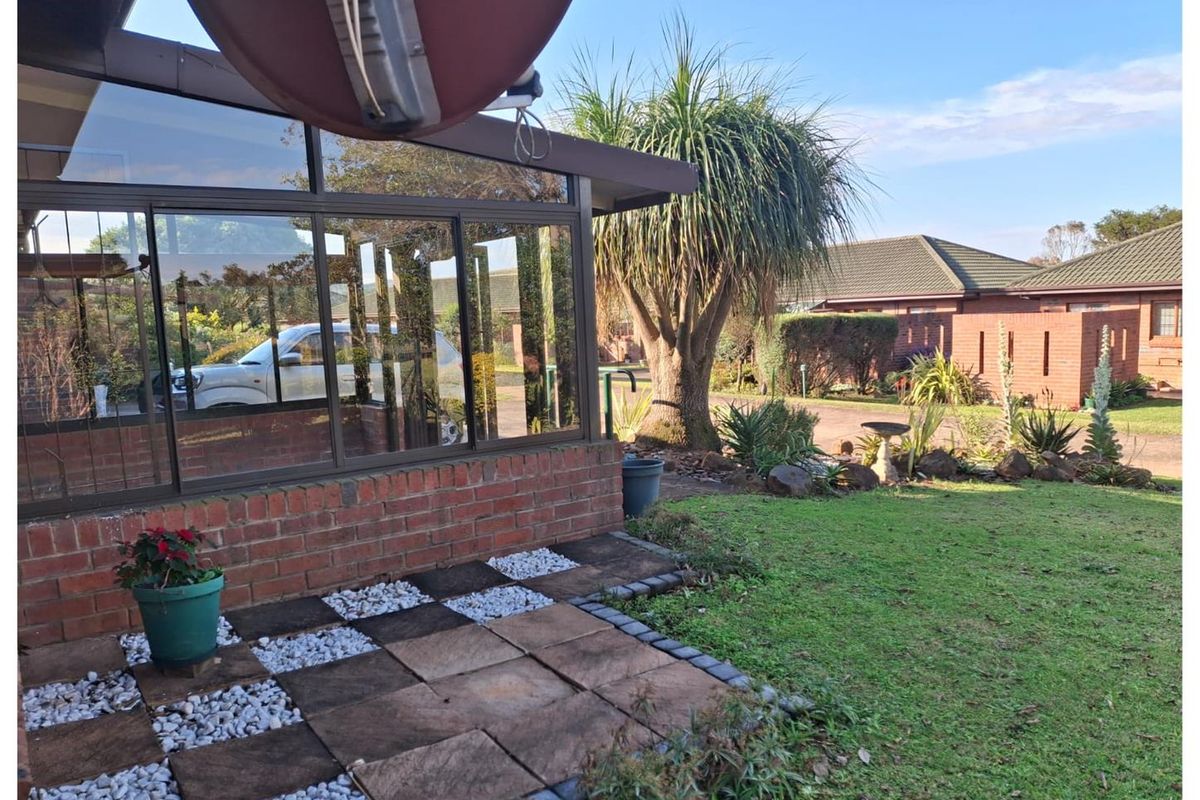 A view of the exterior rear garden featuring a paved patio area, brick facade, and established landscaping.