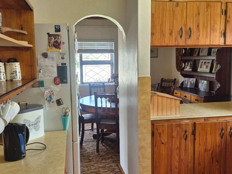 A dated kitchen featuring traditional wooden cabinetry, laminate countertops, and a tiled backsplash, with an arched doorway leading to the adjacent dining area.