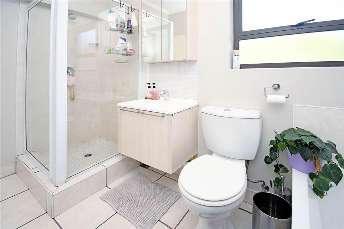 A functional bathroom featuring a glass-enclosed shower, a wall-mounted vanity with basin, a mirrored medicine cabinet, and tiled flooring.