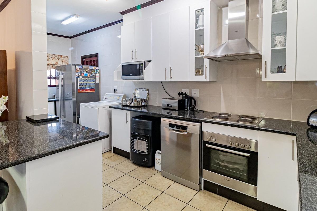 A functional kitchen featuring granite countertops, white cabinetry, a built-in oven with electric hob, and a stainless steel extractor fan.