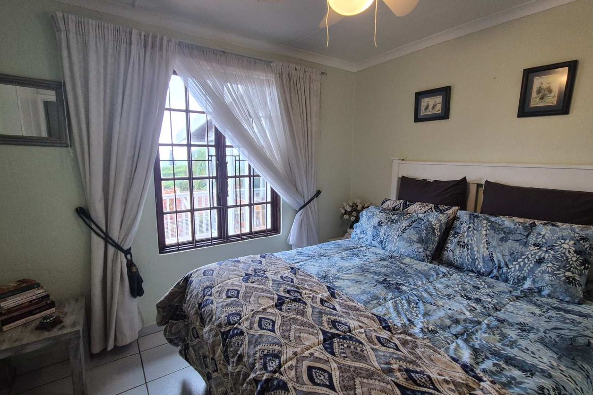 A cozy bedroom featuring tiled flooring, a ceiling fan, and a window with security bars, offering a functional and comfortable living space.
