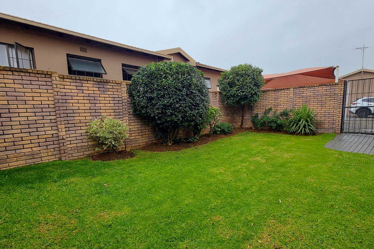 A private rear garden featuring a well-maintained lawn, established shrubs, and a secure brick boundary wall with a metal pedestrian gate.