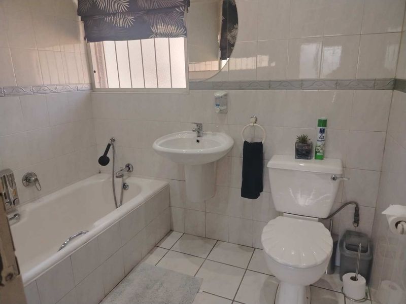 A functional bathroom featuring a pedestal basin, bathtub with handheld shower, and tiled finishes throughout.