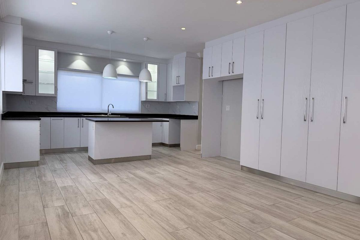 A modern, spacious kitchen featuring white cabinetry, a central island, stone countertops, and wood-look tile flooring in an open-plan layout.