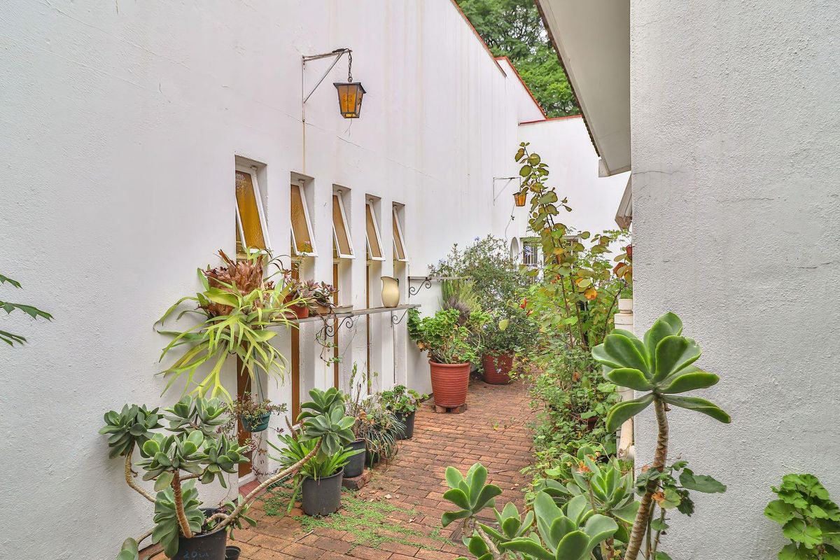 A narrow exterior side passage featuring a brick-paved walkway, white rendered walls, and a series of vertical awning windows.