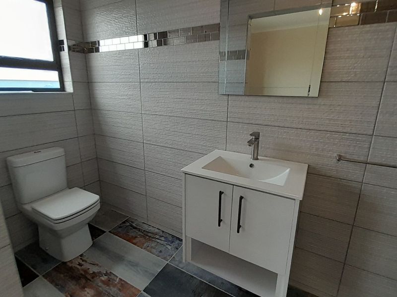 A modern, well-maintained bathroom featuring tiled walls and flooring, a contemporary vanity with basin, and a wall-mounted mirror.