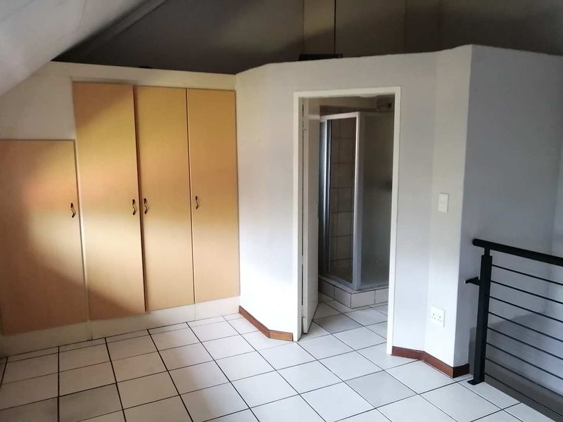 An empty bedroom featuring tiled flooring, built-in cupboards, and an en-suite shower room with a metal balustrade overlooking the lower level.