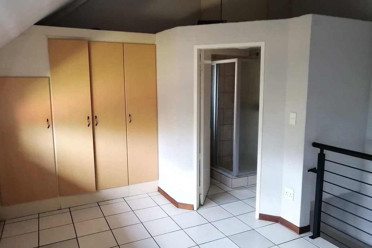 An empty bedroom featuring tiled flooring, built-in cupboards, and an en-suite shower room with a metal balustrade overlooking the lower level.