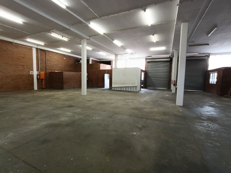 Spacious industrial warehouse unit featuring exposed brick walls, concrete flooring, high ceilings with strip lighting, and dual roller shutter doors for easy access.