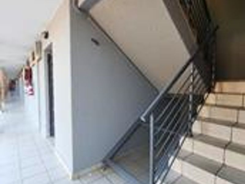 An outdoor apartment complex hallway featuring a tiled walkway and a metal staircase with a matching balustrade.