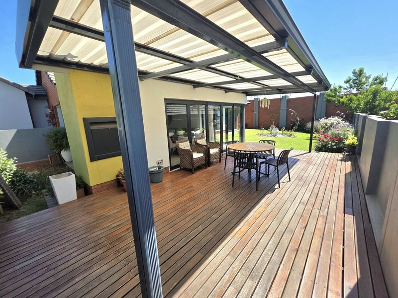Spacious outdoor patio featuring timber decking, a covered roof structure, and a built-in fireplace, perfect for alfresco dining and entertaining.