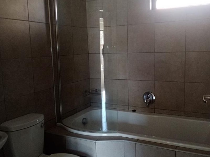 A functional bathroom featuring tiled walls and flooring, a built-in bathtub with a glass shower screen, and a standard toilet.