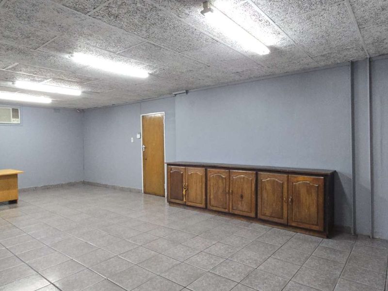 Spacious office area featuring tiled flooring, acoustic ceiling tiles, built-in wooden cabinetry, and wall-mounted air conditioning.