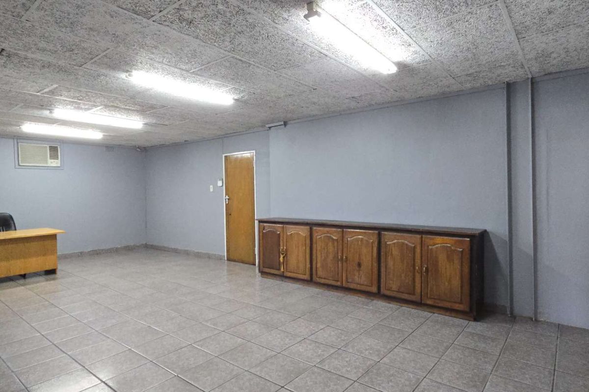Spacious office area featuring tiled flooring, acoustic ceiling tiles, built-in wooden cabinetry, and wall-mounted air conditioning.