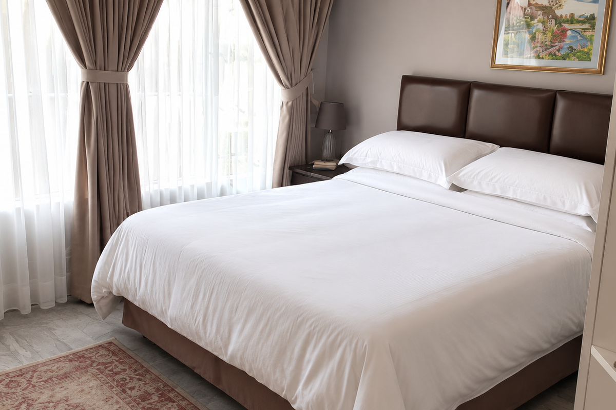 A well-maintained bedroom featuring tiled flooring, neutral wall tones, and built-in shelving, complemented by large windows with elegant drapery.
