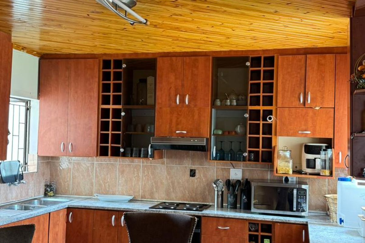 A functional kitchen featuring wood-toned cabinetry, tiled backsplash, integrated hob and extractor fan, and a distinctive wood-paneled ceiling.