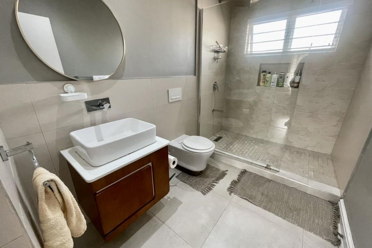 Modern bathroom featuring a vessel sink on a wooden vanity, wall-hung toilet, and a spacious walk-in shower with a recessed niche and glass screen.