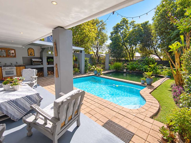 Covered patio area featuring a built-in braai, overlooking a swimming pool and landscaped garden.
