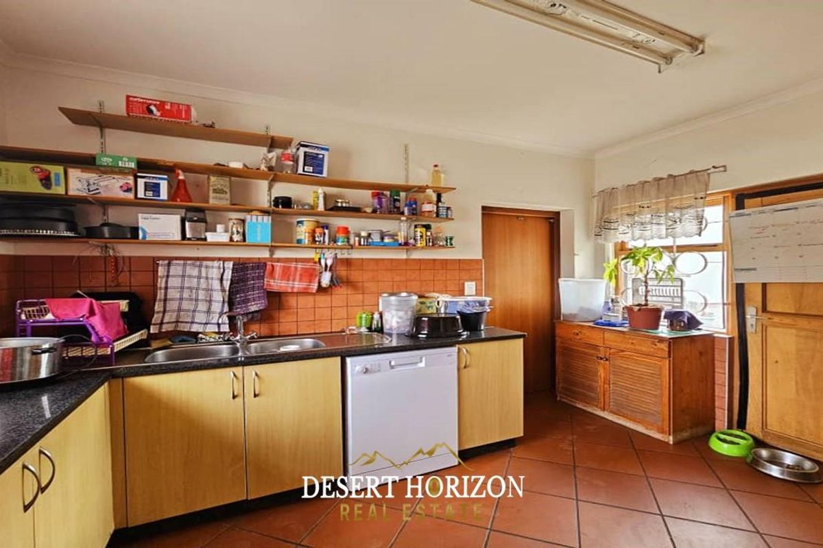 A dated kitchen featuring laminate cabinetry, open shelving, a double basin sink, and terracotta floor tiles, offering potential for a modern renovation.