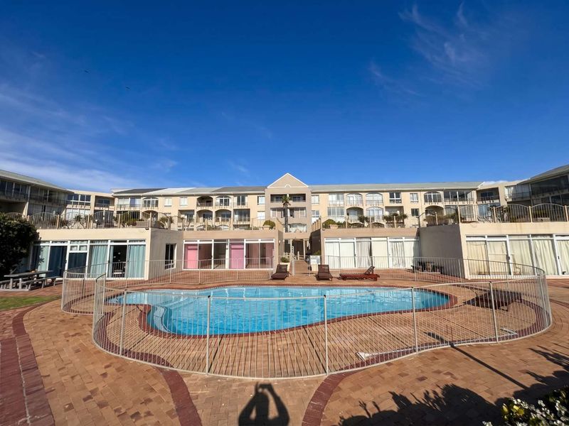 A well-maintained apartment complex featuring a central swimming pool with secure metal fencing and paved surround, overlooked by multiple residential balconies.