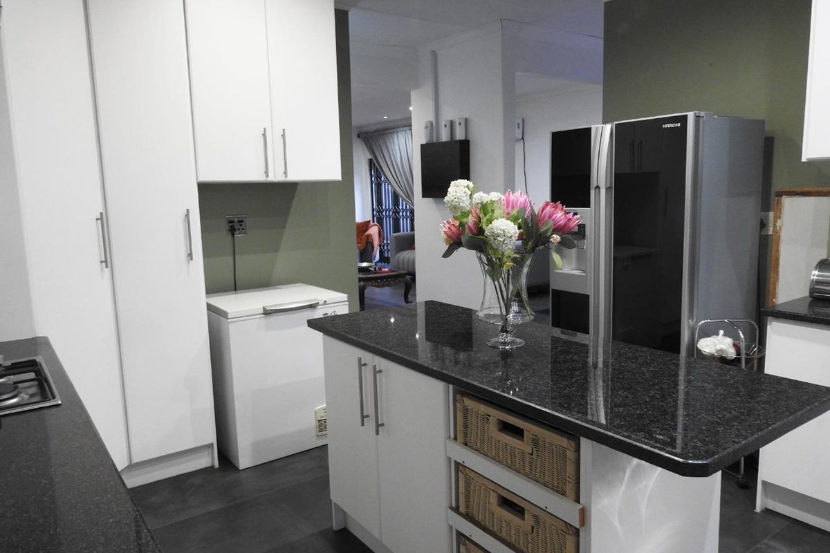 Modern kitchen featuring white cabinetry, dark granite countertops, a central island, and tiled flooring, with an open-plan flow into the adjacent living area.