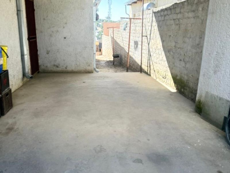 A covered outdoor patio area featuring concrete flooring, a corrugated metal roof, and stone masonry walls, offering potential for an outdoor entertainment space.
