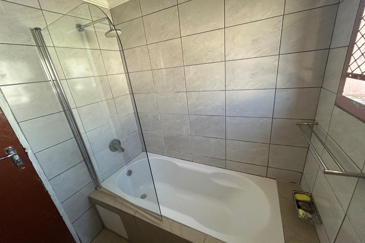 A functional bathroom featuring a built-in bathtub with a glass shower screen and full-height wall tiling.